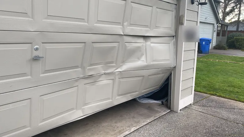 Garage door with dented and buckled panels after a car hit it